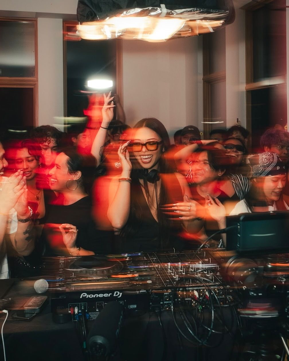 Ein DJ und tanzende Gäste im warmen Licht